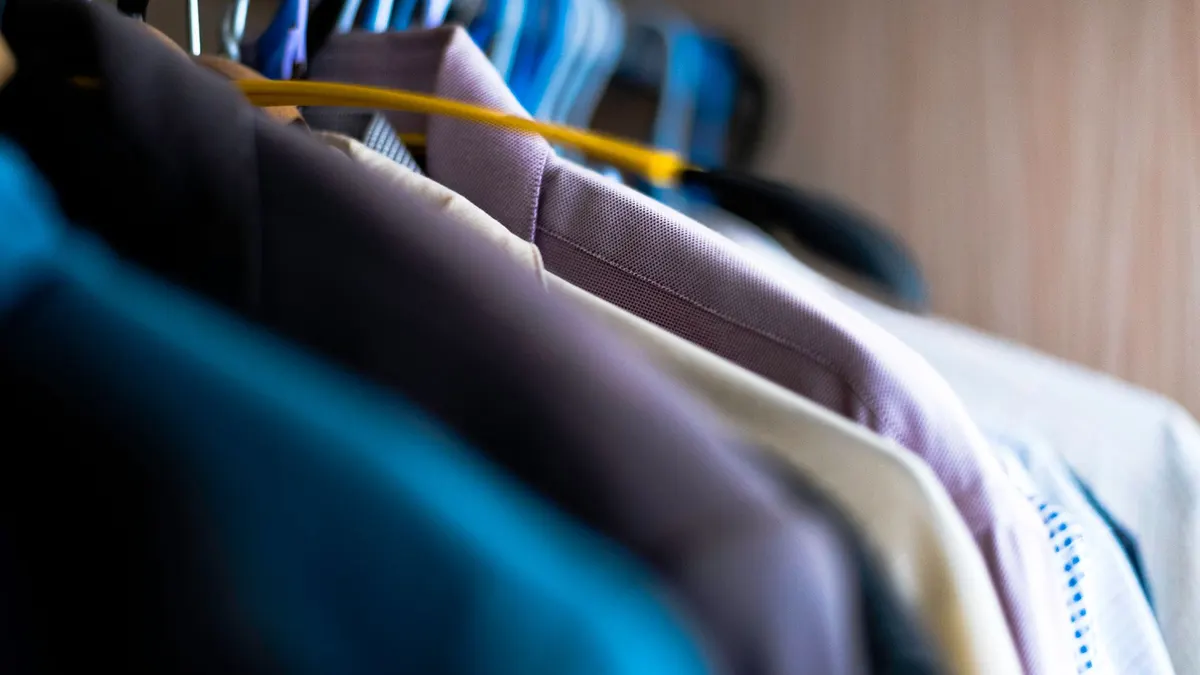 Close-up of various shirts hanging on colorful hangers inside a wardrobe.