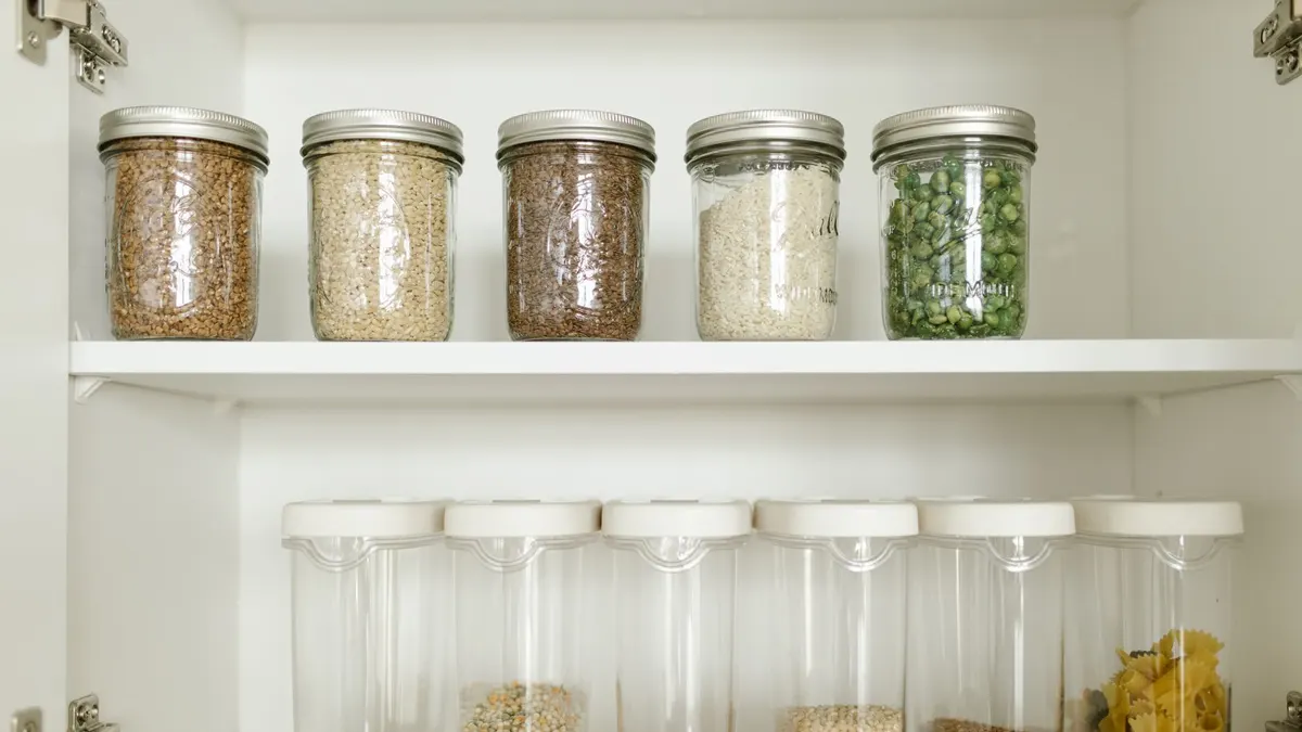 Neatly arranged pantry showcasing grains in glass jars and dry goods in plastic containers.