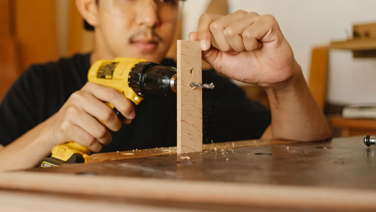 Crop anonymous ethnic male drilling timber detail for making holes while working on table in workshop