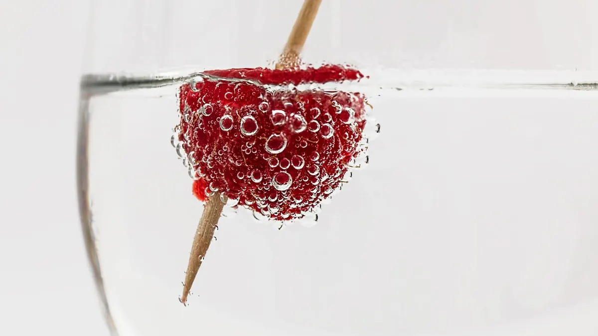 Close-up of a raspberry in sparkling water, highlighting freshness and effervescence.
