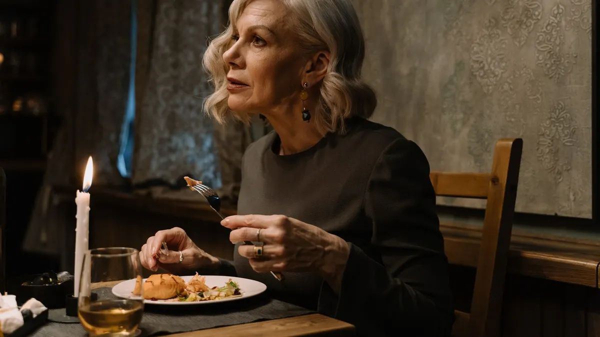 Senior woman enjoying a candlelit dinner in an elegant setting.