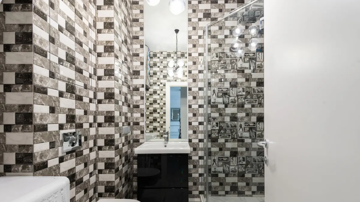 Interior of bright washroom with washing machine near toilet next to shower and sink with tap