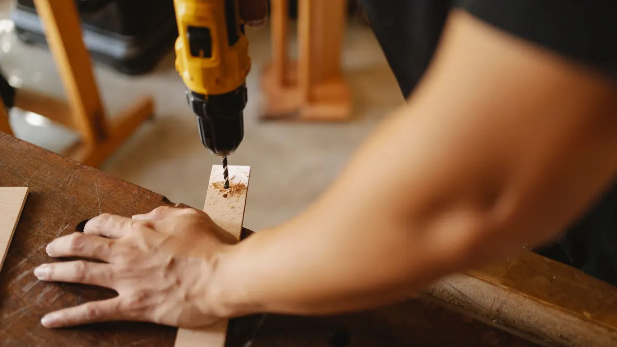 Crop anonymous male fixing wooden plank and drilling hole while working on table in workshop