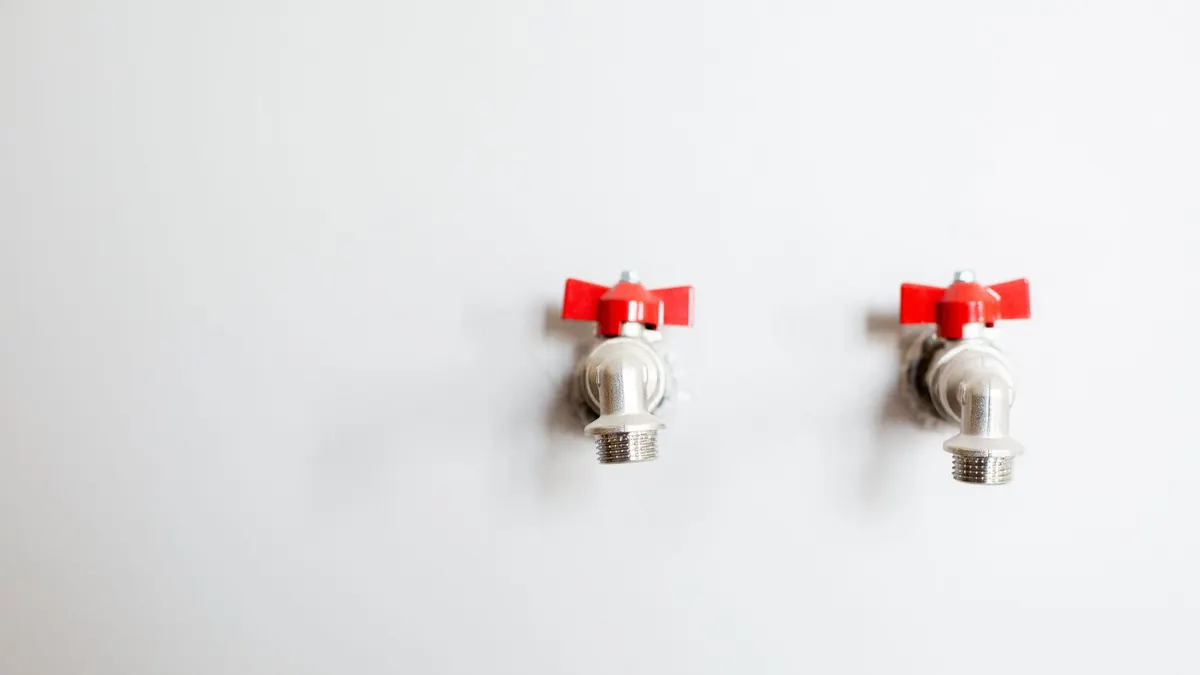 Close-up of two metal faucets with red handles against a white wall, showcasing plumbing detail.