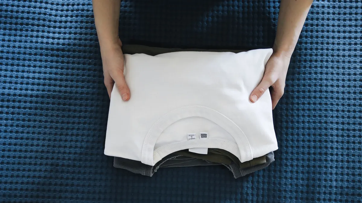 Hands folding a white shirt on a blue textured bedspread, focusing on organizing clothes.