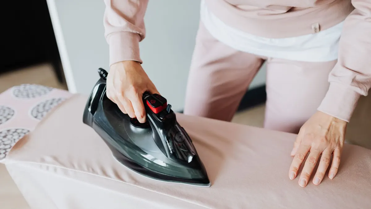 Adult woman ironing clothing on board using a black iron in an indoor setting.