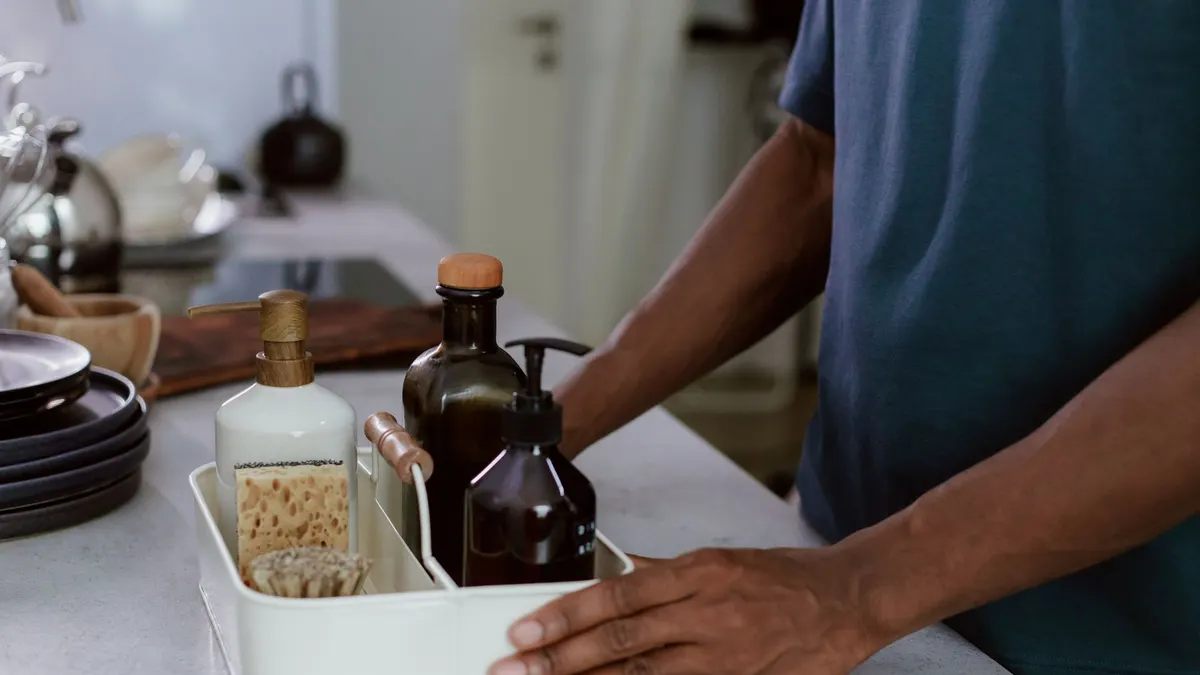 A close-up of a man organizing cleaning products in a modern kitchen environment.
