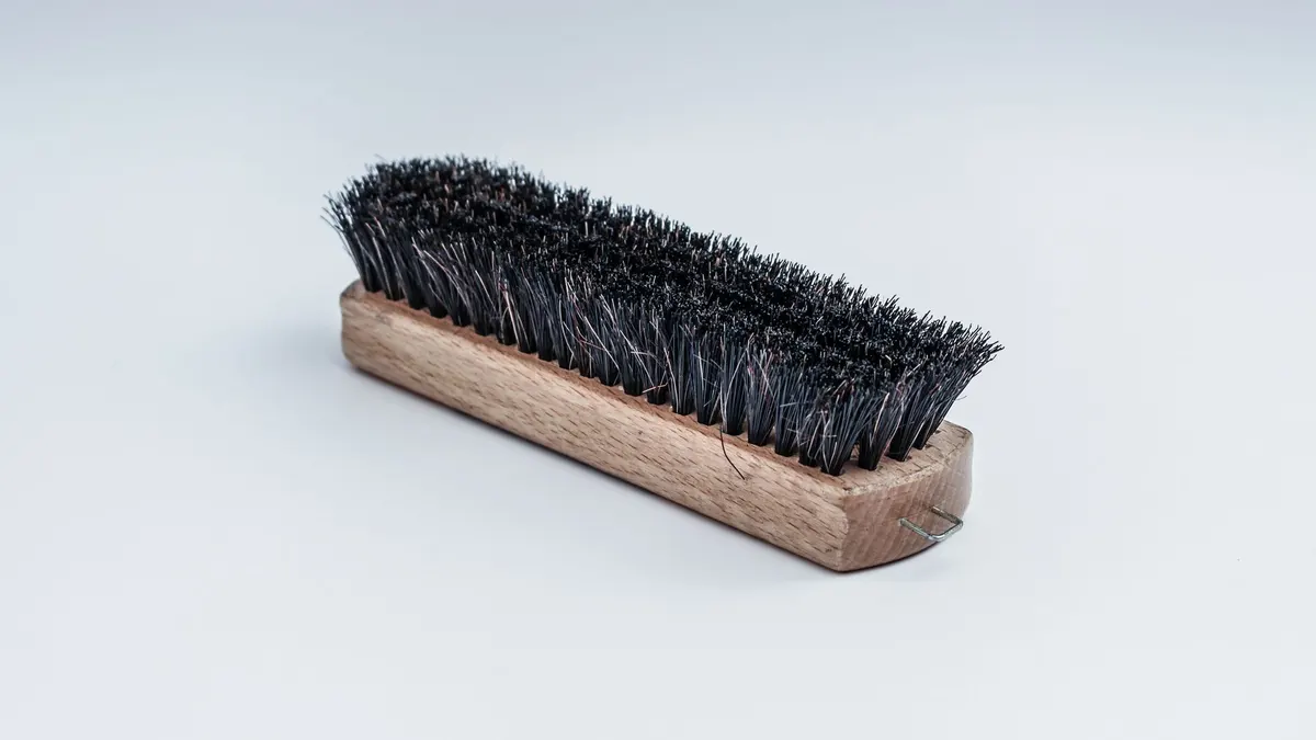 Close-up of a wooden cleaning brush with dense black bristles on a white background.