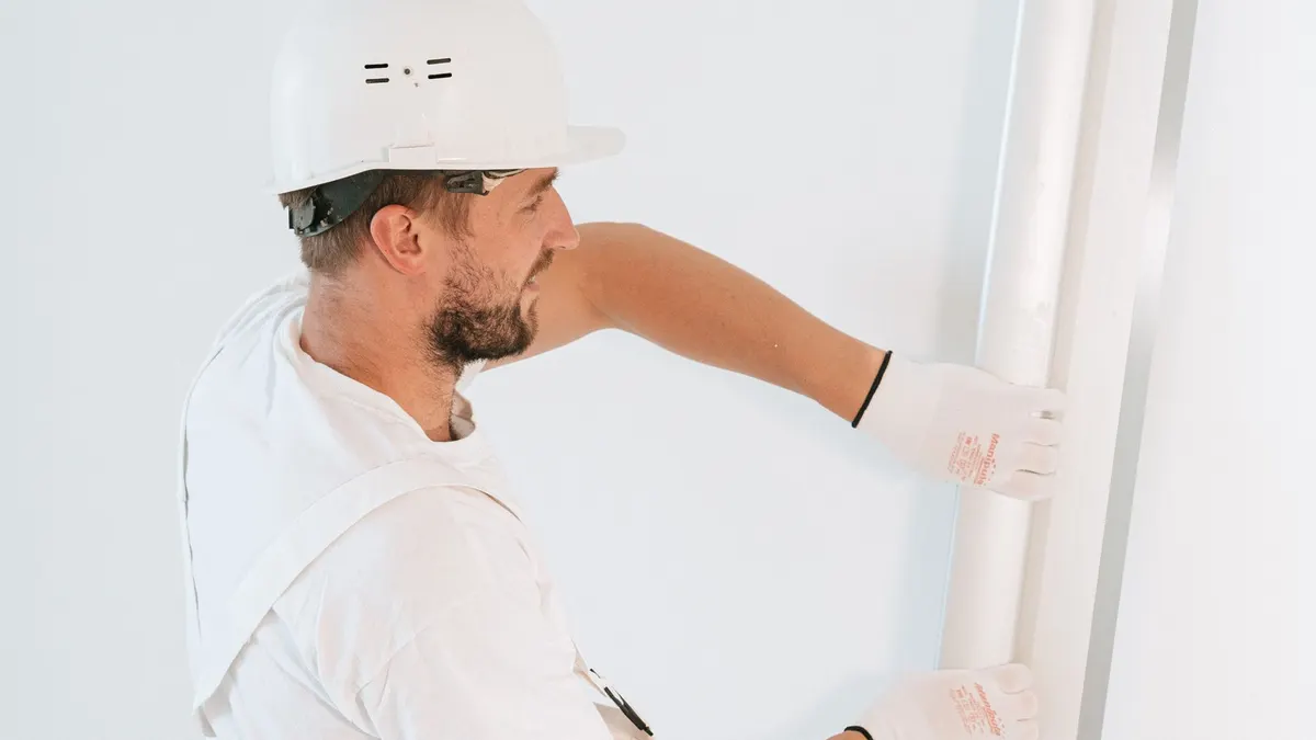 Professional construction worker installing drywall with gloves and helmet inside a building.