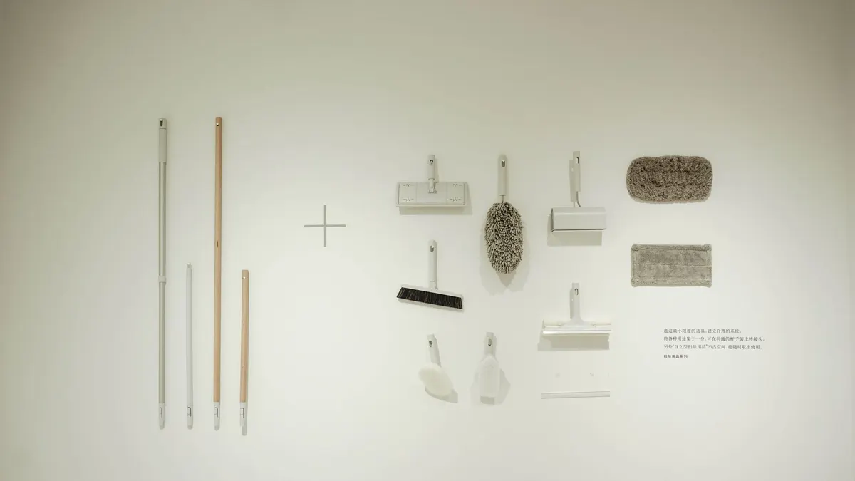 A minimalist flat lay of various cleaning tools arranged on a white wall, showcasing a modern concept.