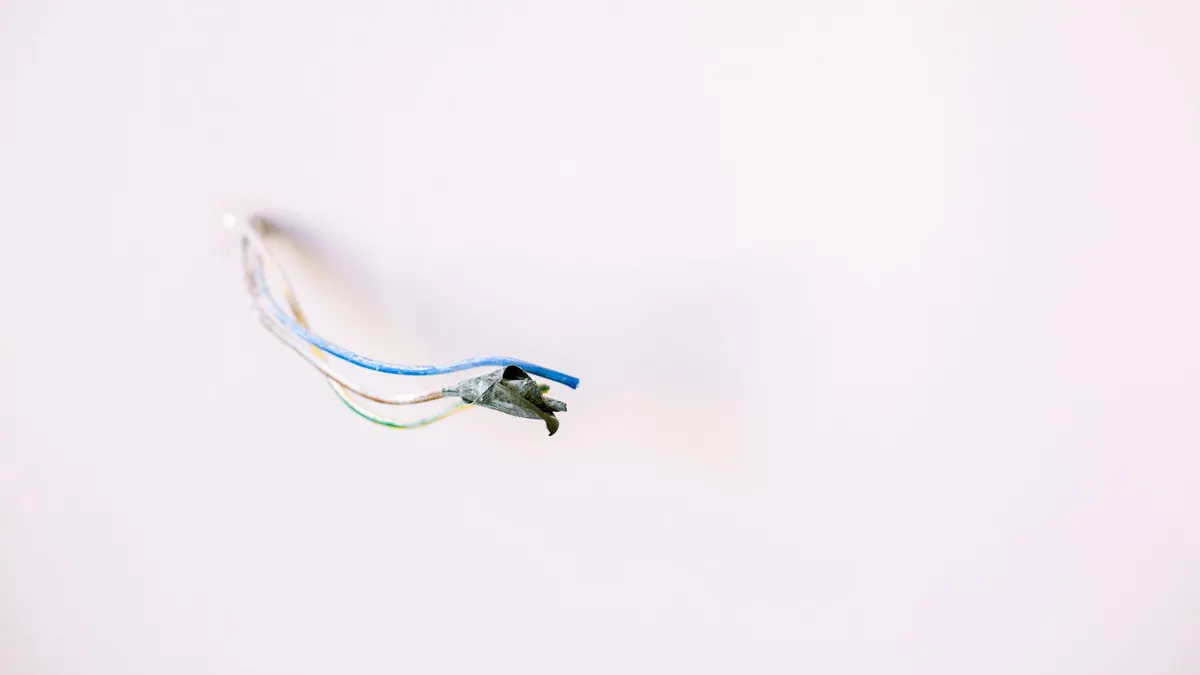 Loose electrical wires protruding from a white wall, ideal for home improvement concepts.