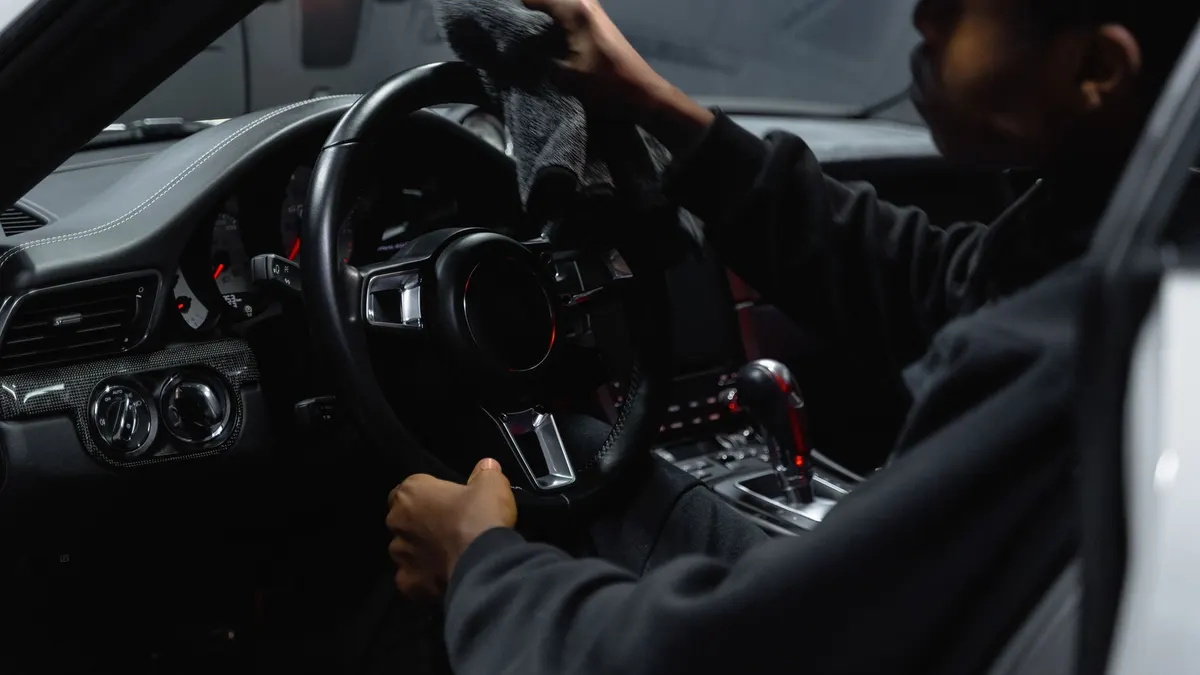 Adult man wiping a car steering wheel with a cloth inside a vehicle.