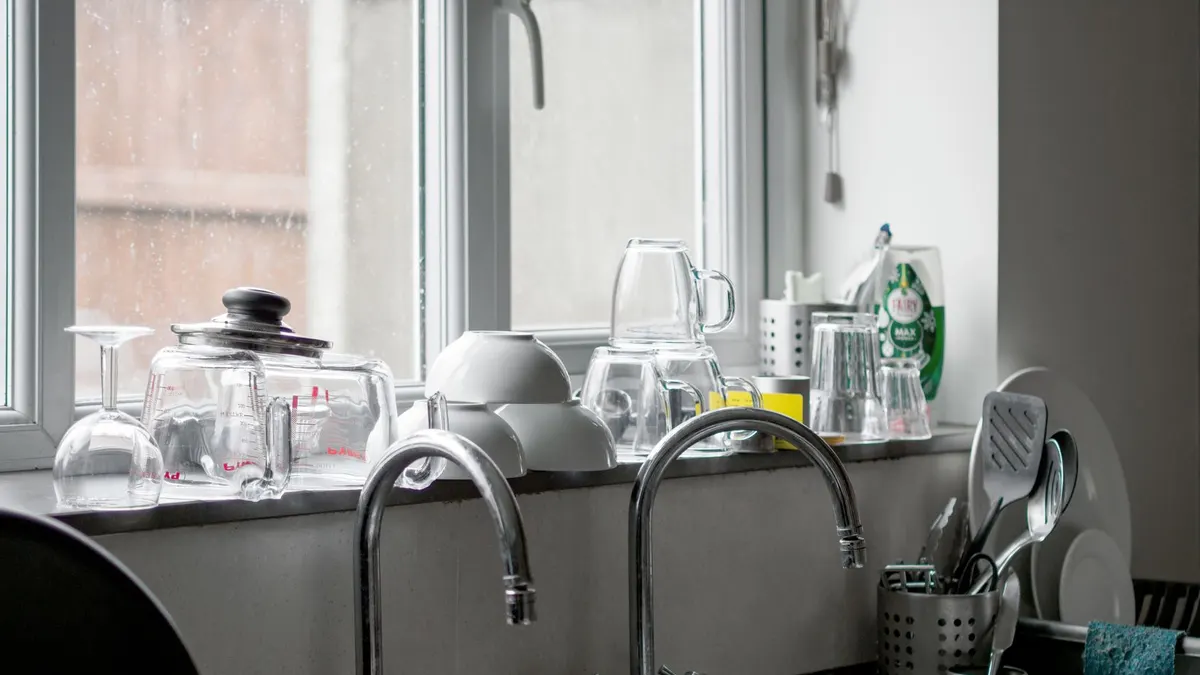 Contemporary kitchen featuring a stainless steel sink with kitchenware and glassware on the windowsill.