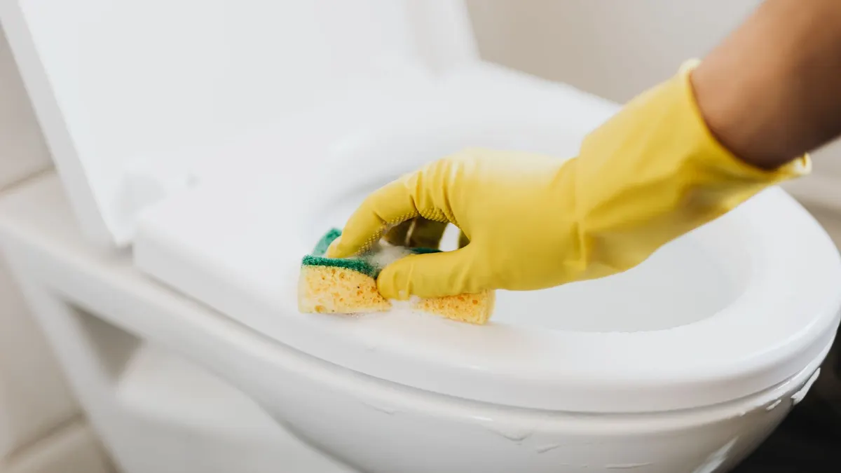 From above of crop anonymous person in rubber gloves using soapy sponge while cleaning toilet bowl