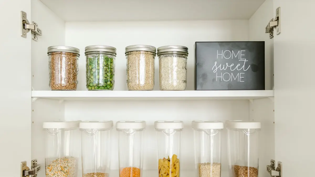 Neatly arranged glass and plastic jars containing grains and pasta in a kitchen cabinet.