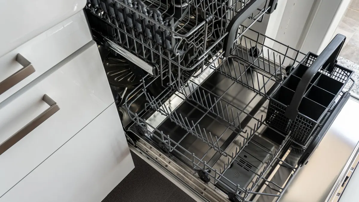 A clean and empty stainless steel dishwasher open in a modern kitchen setting.