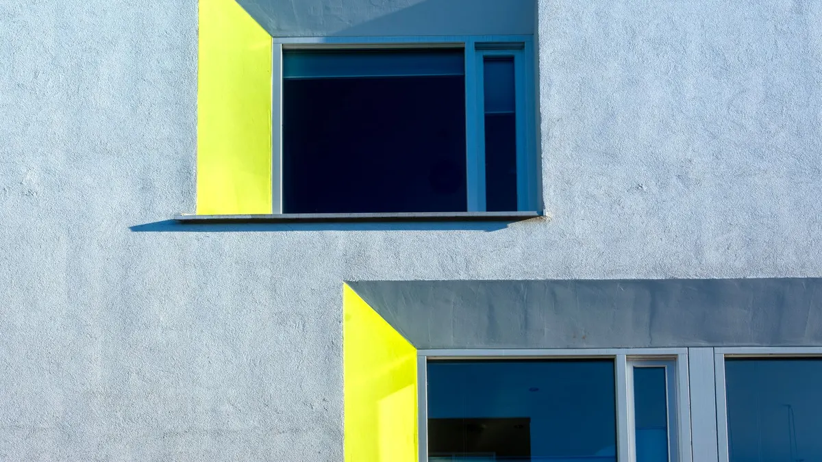 Minimalist architecture featuring vibrant yellow and blue window accents on a textured facade.