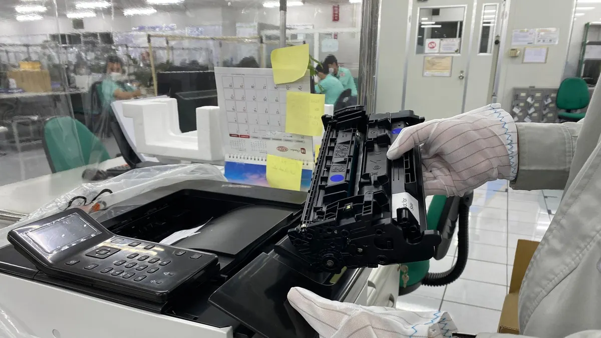 Worker replacing printer ink cartridge in a laboratory environment, highlighting technology maintenance.
