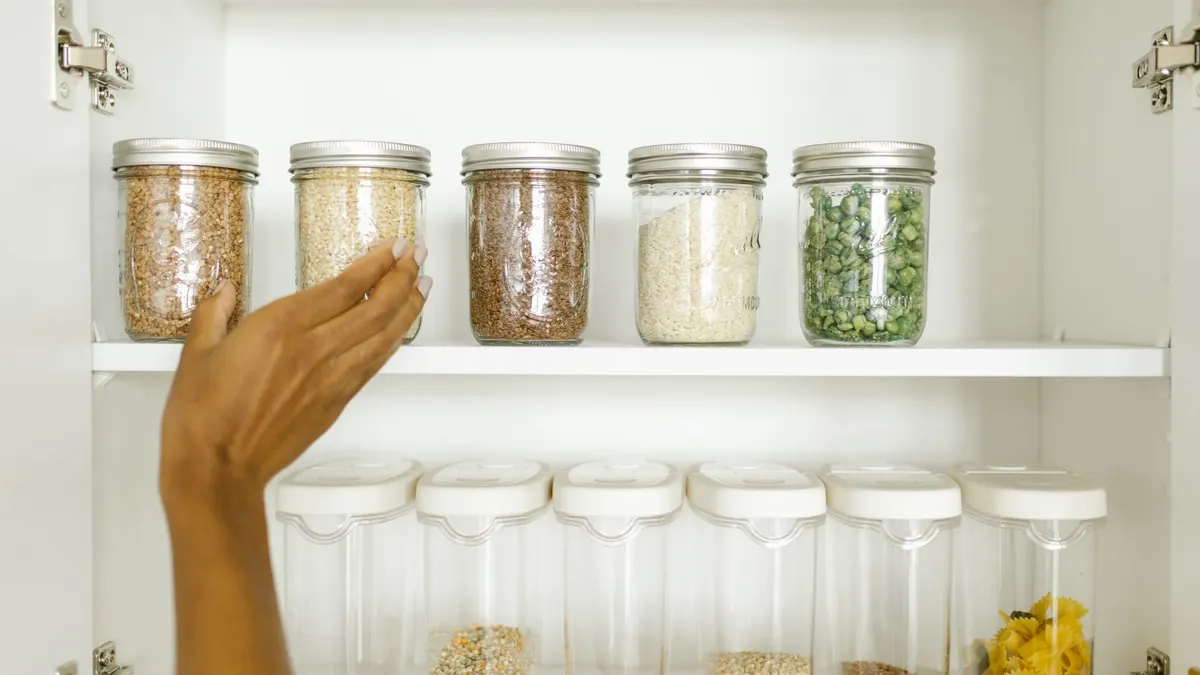 A neat pantry shelf showing various grains stored in labeled glass and plastic containers, promoting kitchen organization.