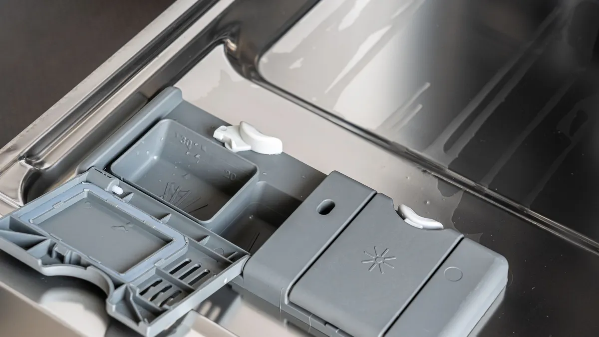 A detailed view of a dishwasher detergent compartment with soap residue.
