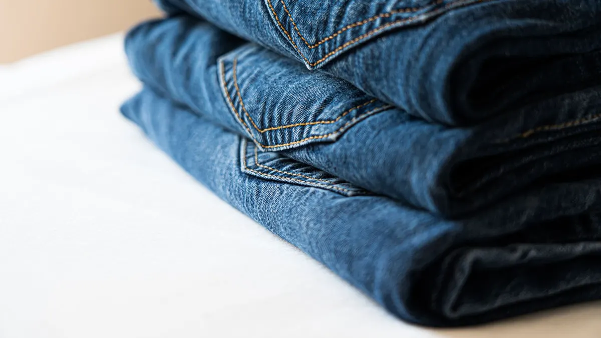 Stack of neatly folded blue denim jeans highlighting stitching details.