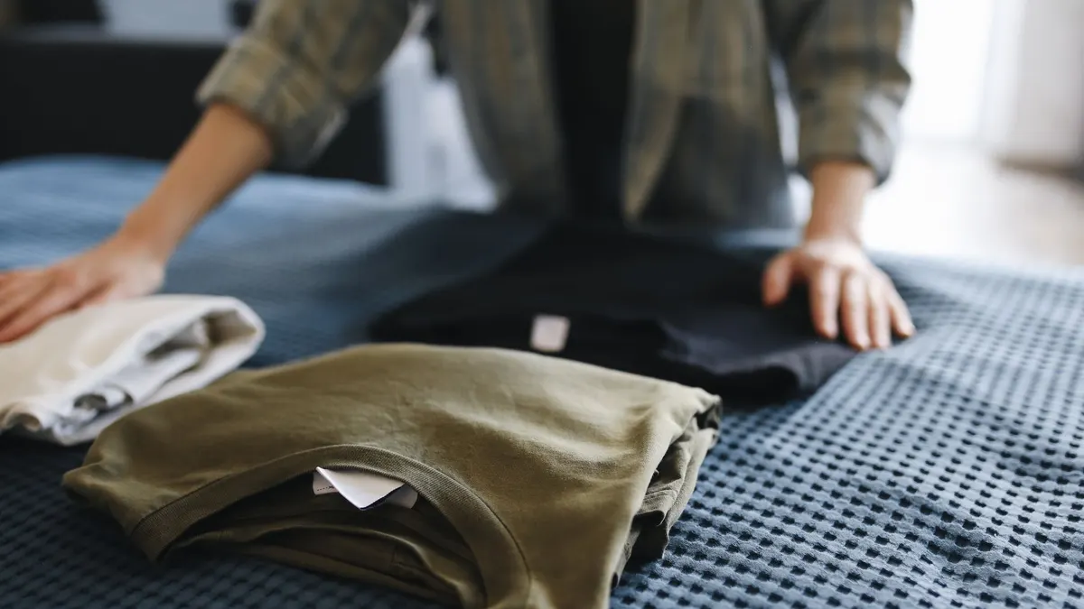 Hands folding T-shirts on a bed, showcasing household chores and casual apparel.