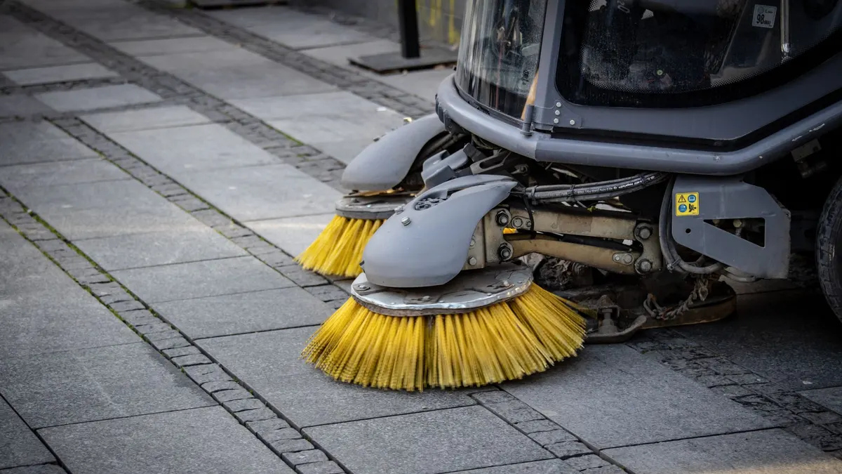 Close-up view of a road sweeper's yellow brushes on a paved street.