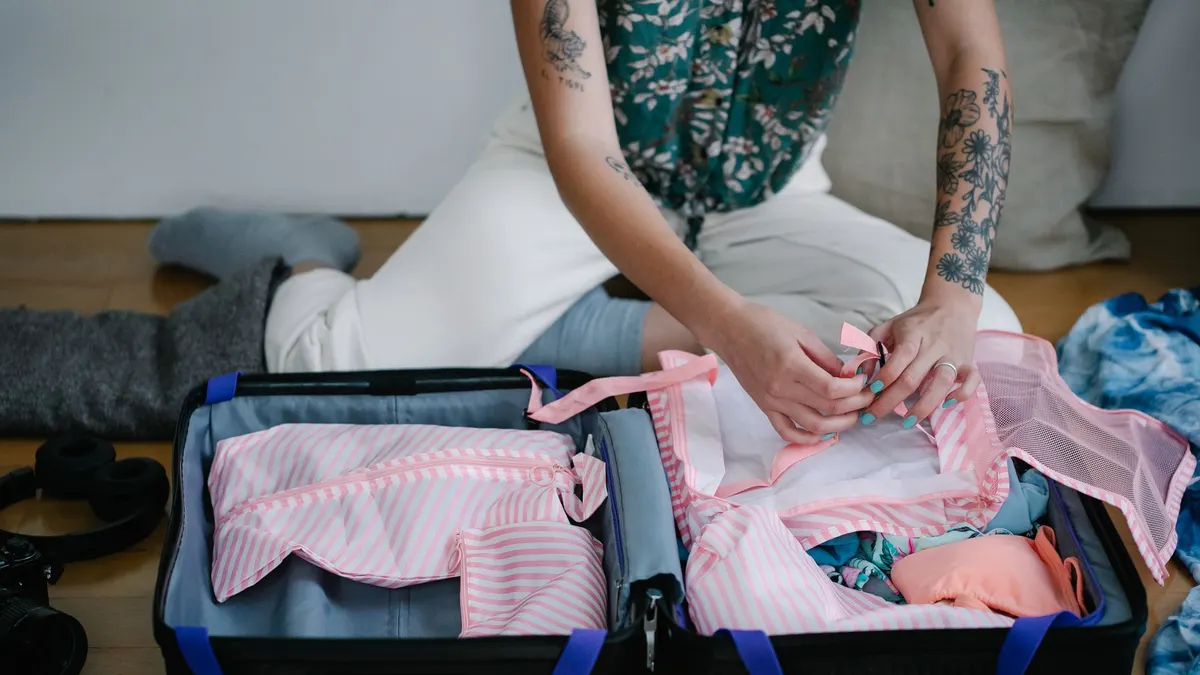 A woman packing her travel suitcase on the floor indoors, preparing for a trip.
