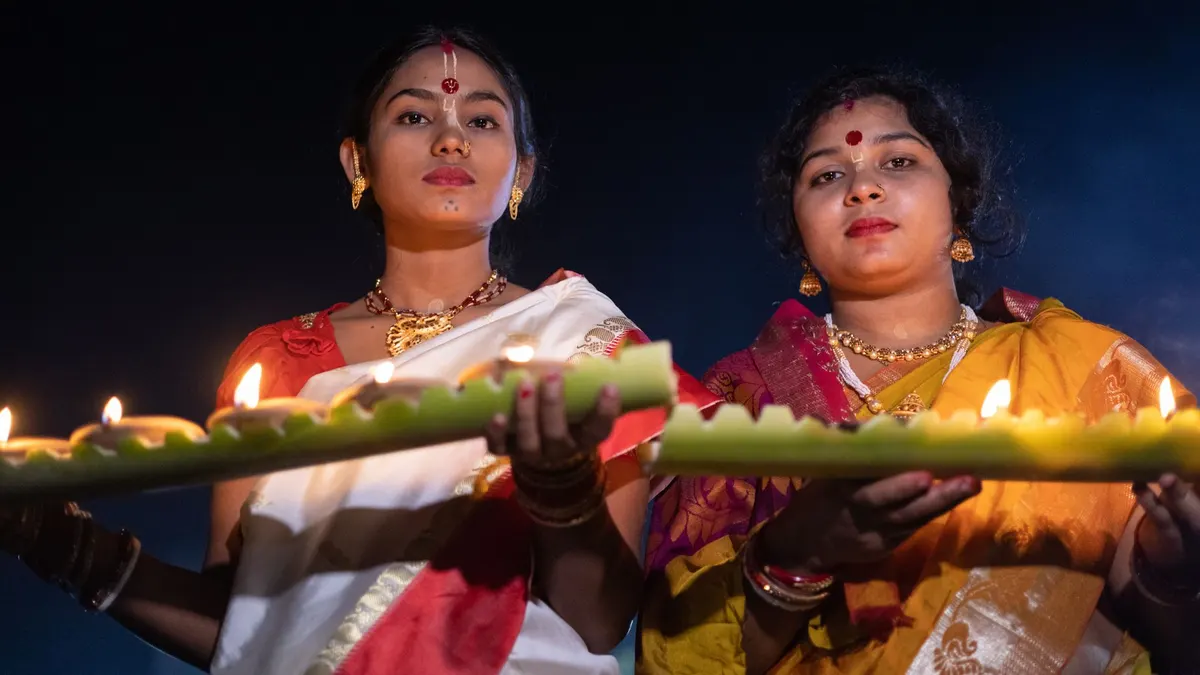 Two women in traditional attire holding candle-lit offerings during a cultural festival.