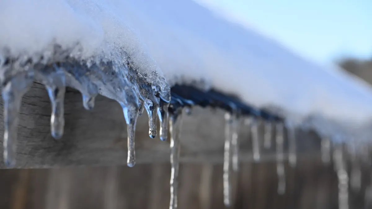 Detailed view of icicles hanging from a snow-covered wooden roof in winter.