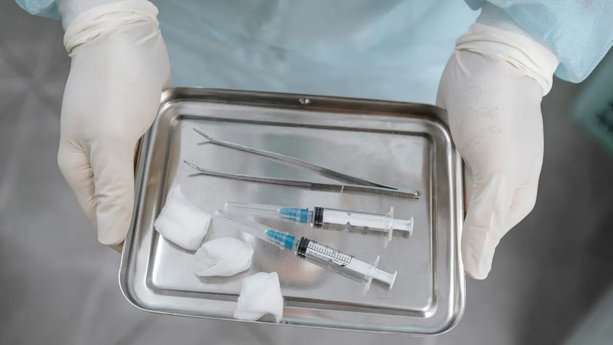 Close-up of a medical professional with syringes, tweezers, and gauze on a steel tray.