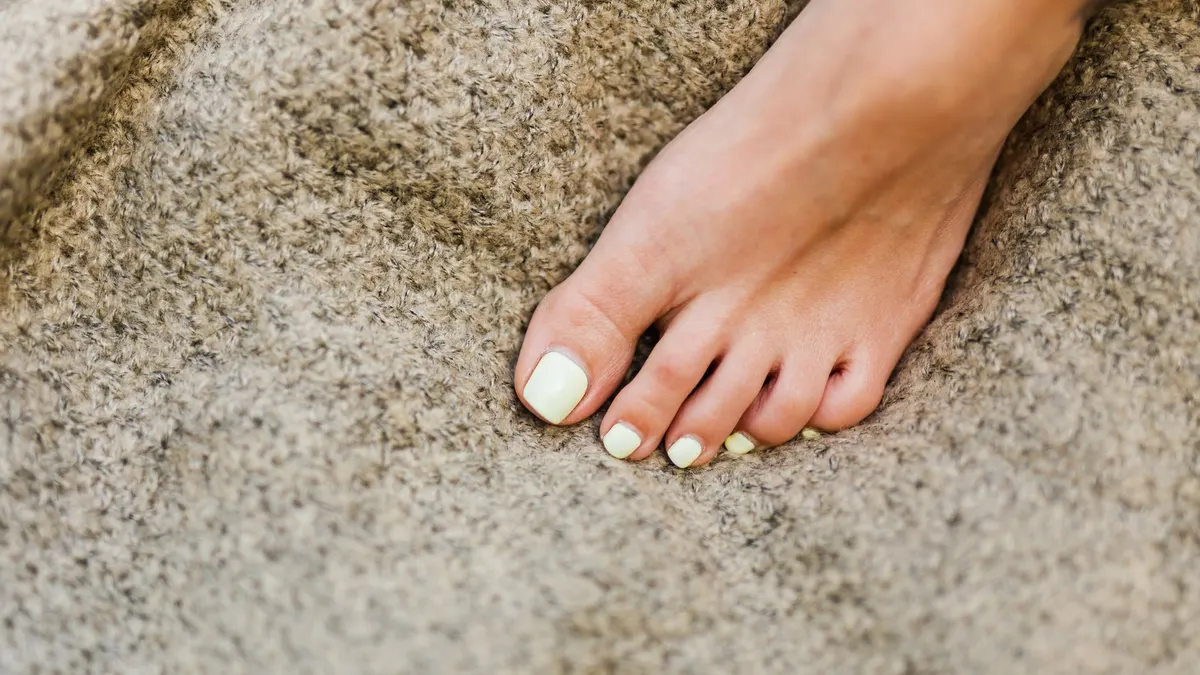 Detailed close-up of a woman's foot with pastel nail polish resting on a textured fabric surface.