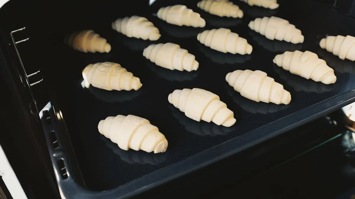 Close-up of raw croissants baking on a tray inside an oven, showcasing homemade pastry preparation.