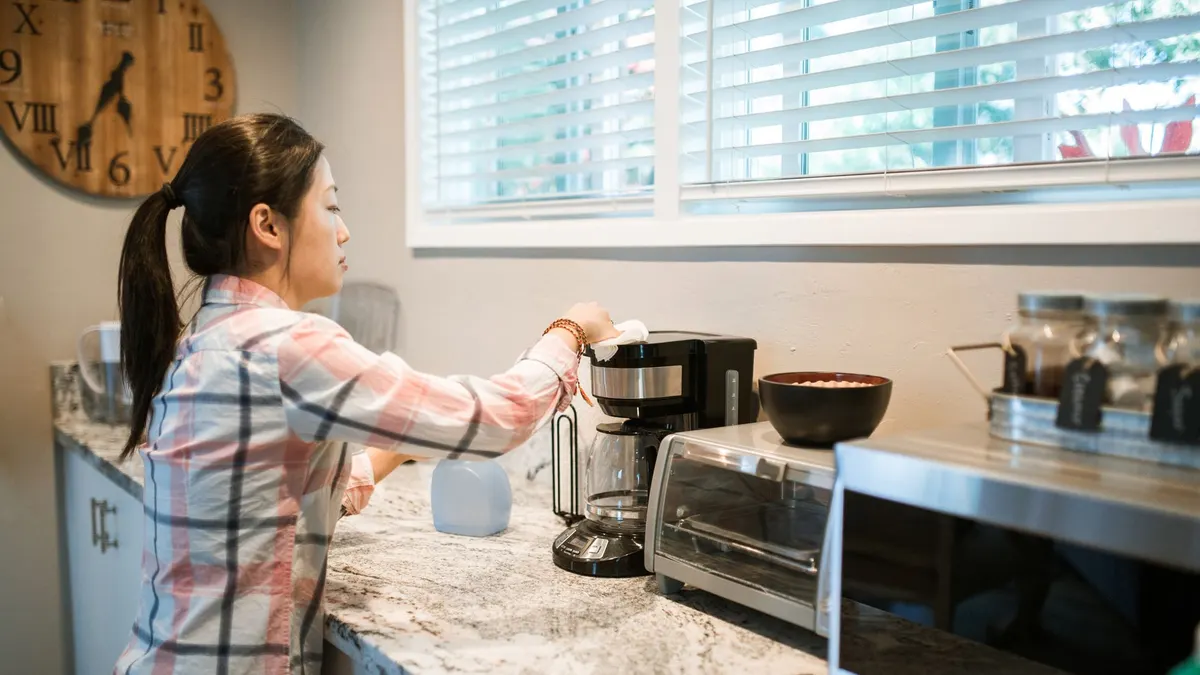 Woman cleaning a coffee maker in a bright, modern kitchen with appliances.