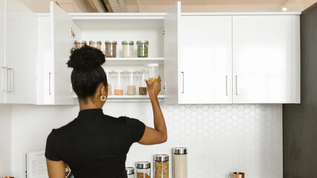 A woman organizing a pantry shelf with various food jars in a modern kitchen.