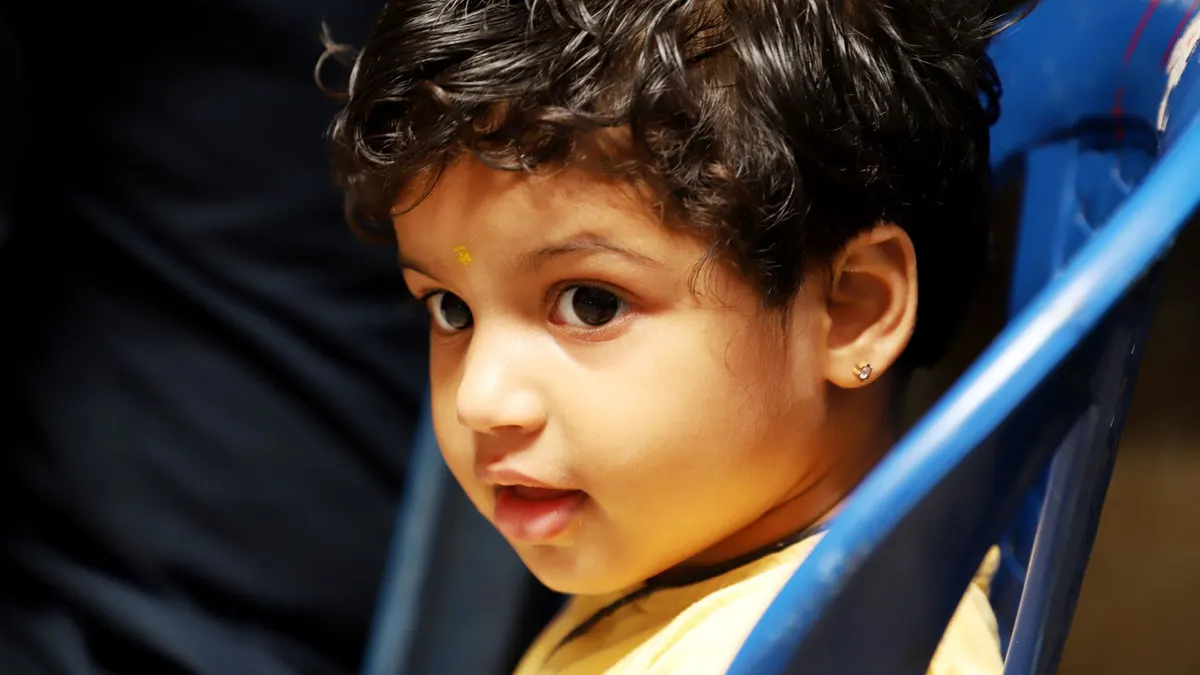 Close-up portrait of a young child with curly hair and curious expression, sitting on a blue chair.