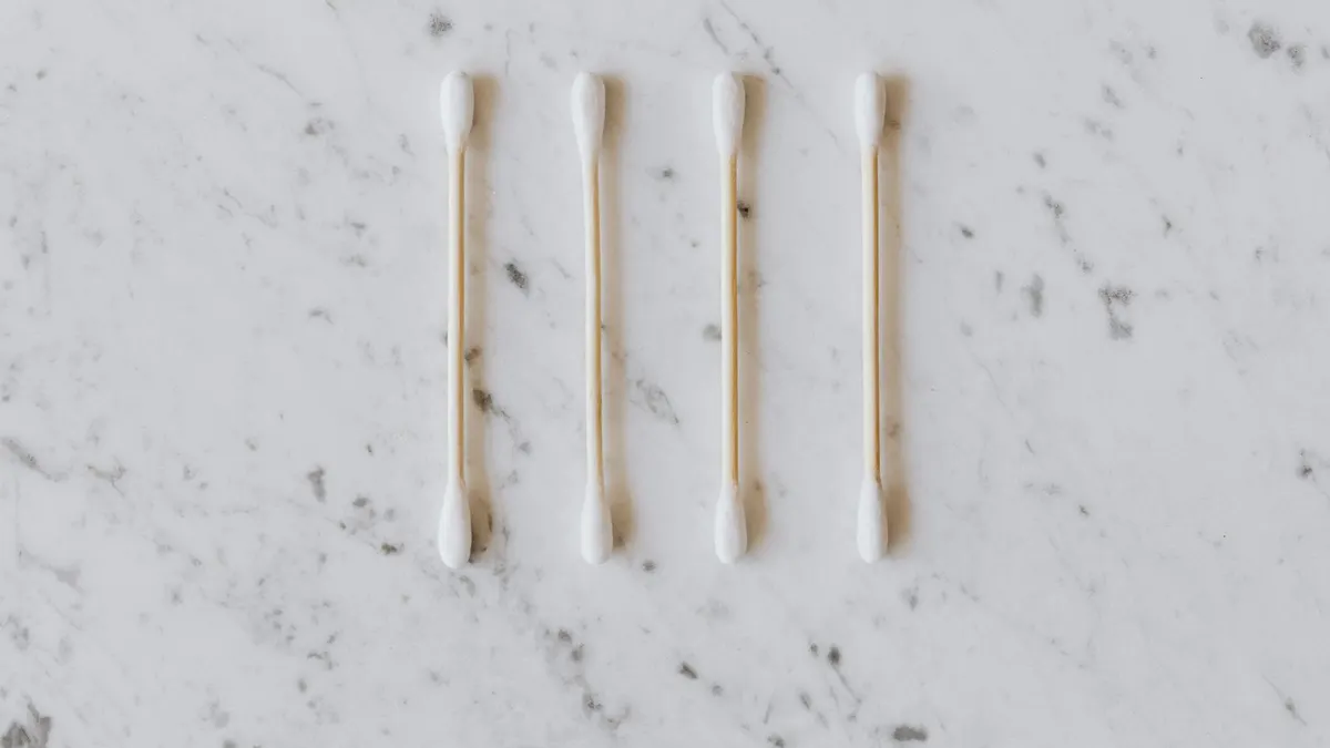 Top view of identical cotton swabs on thin wooden sticks with soft rounded edges on marble surface with tiny spots and gray lines