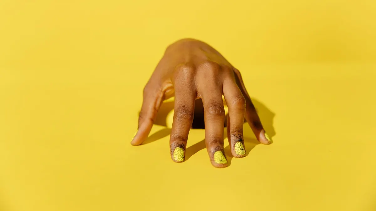 Stylish yellow nail art on a hand against a vibrant yellow background, perfect for beauty and fashion themes.