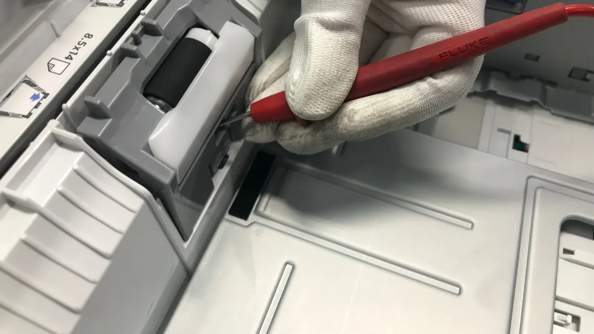A gloved hand fixes a printer using a red precision tool, showcasing maintenance skills.