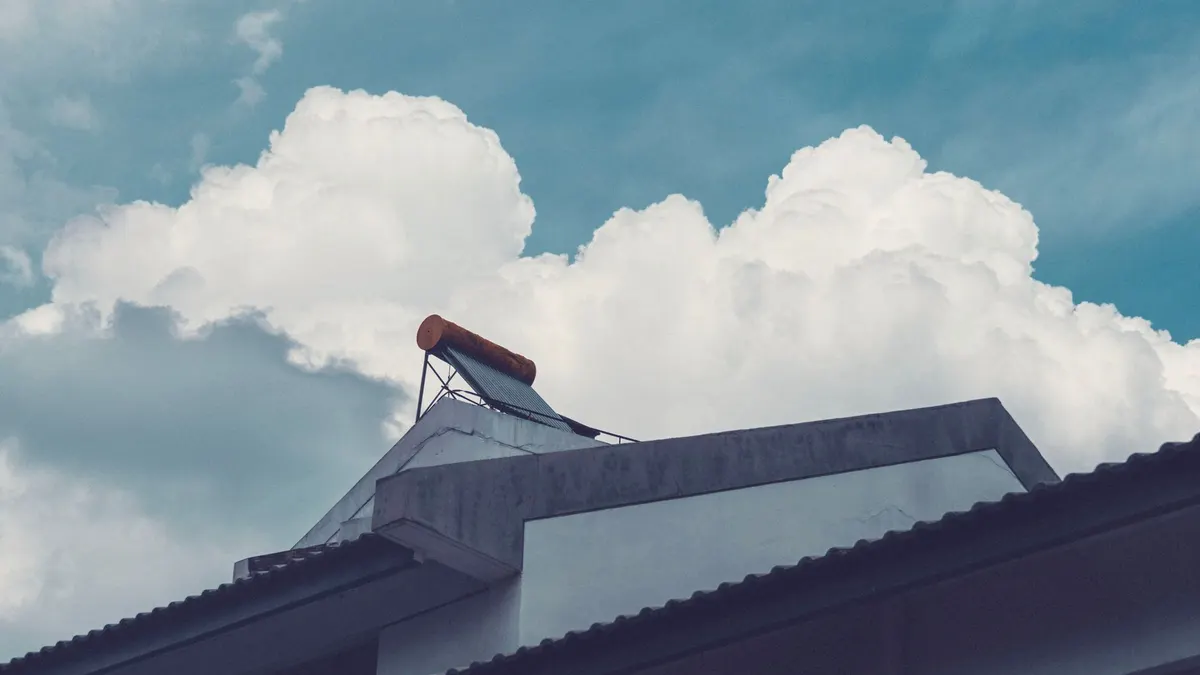 A building rooftop with a solar water heater set against a bright, cloud-filled sky.