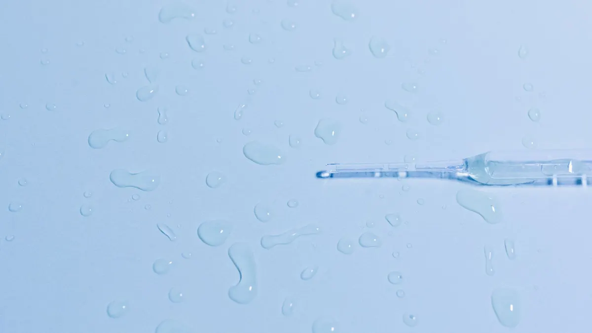 Detailed close-up of a glass pipette on a wet surface with scattered water droplets.