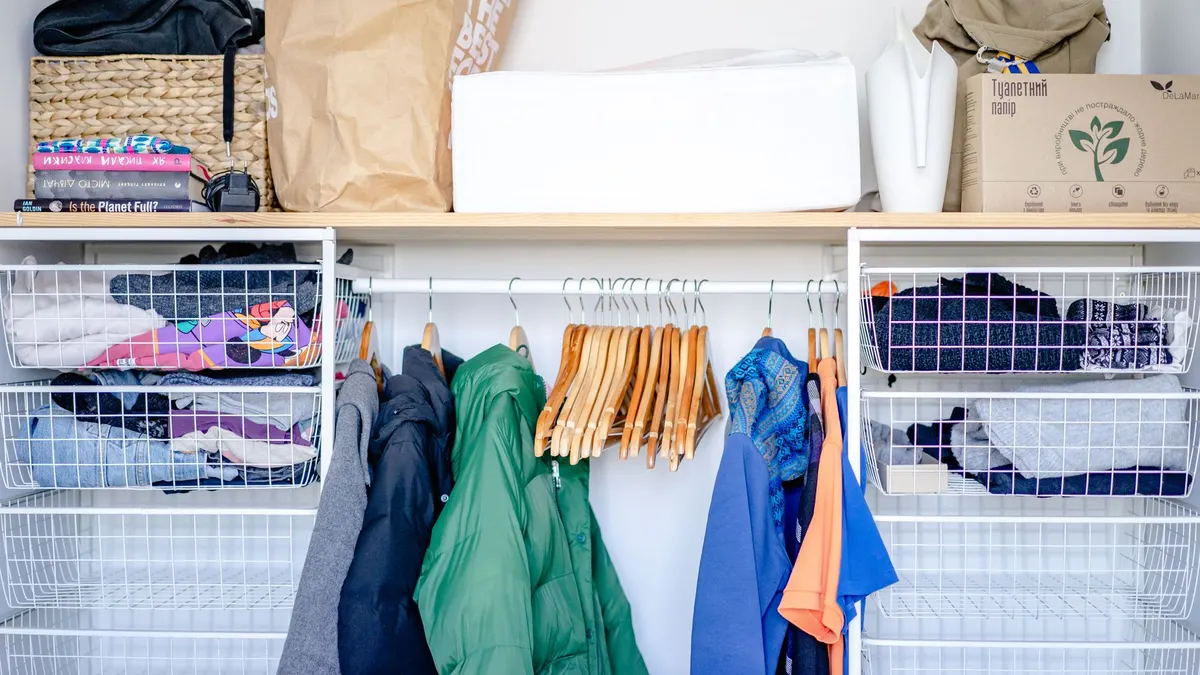 A minimalist open wardrobe featuring modern clothing, hangers, and storage baskets.
