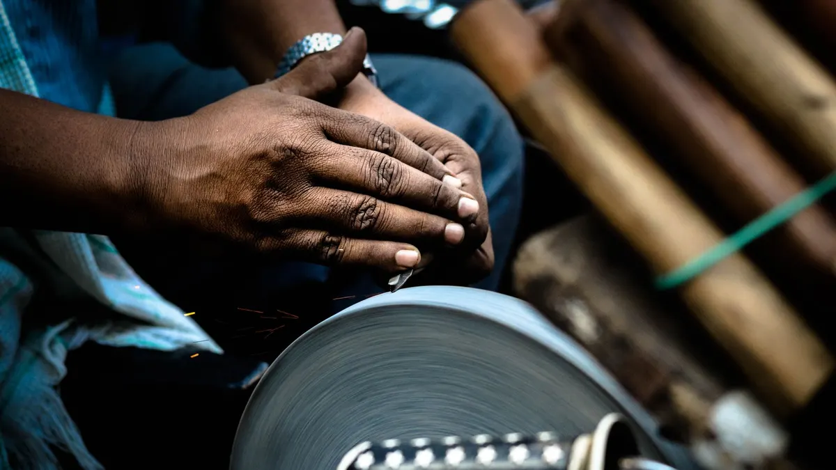 Hands sharpening a knife against a rotating grindstone in a market setting.