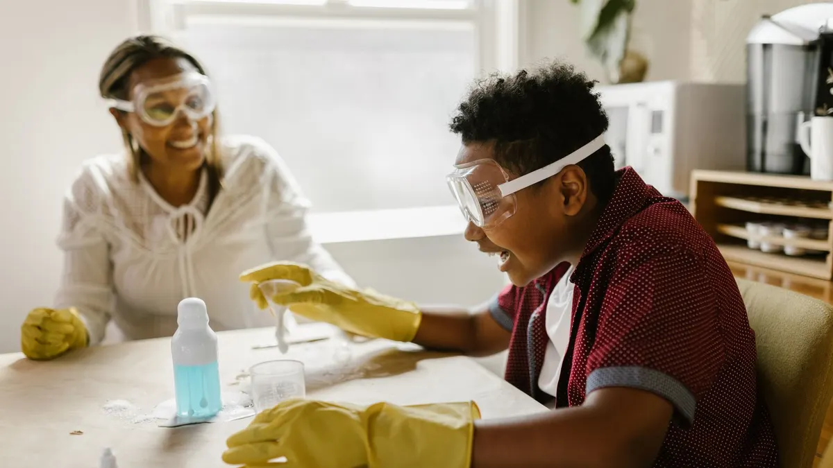 Boy and woman conducting a science experiment at home, wearing gloves and goggles.