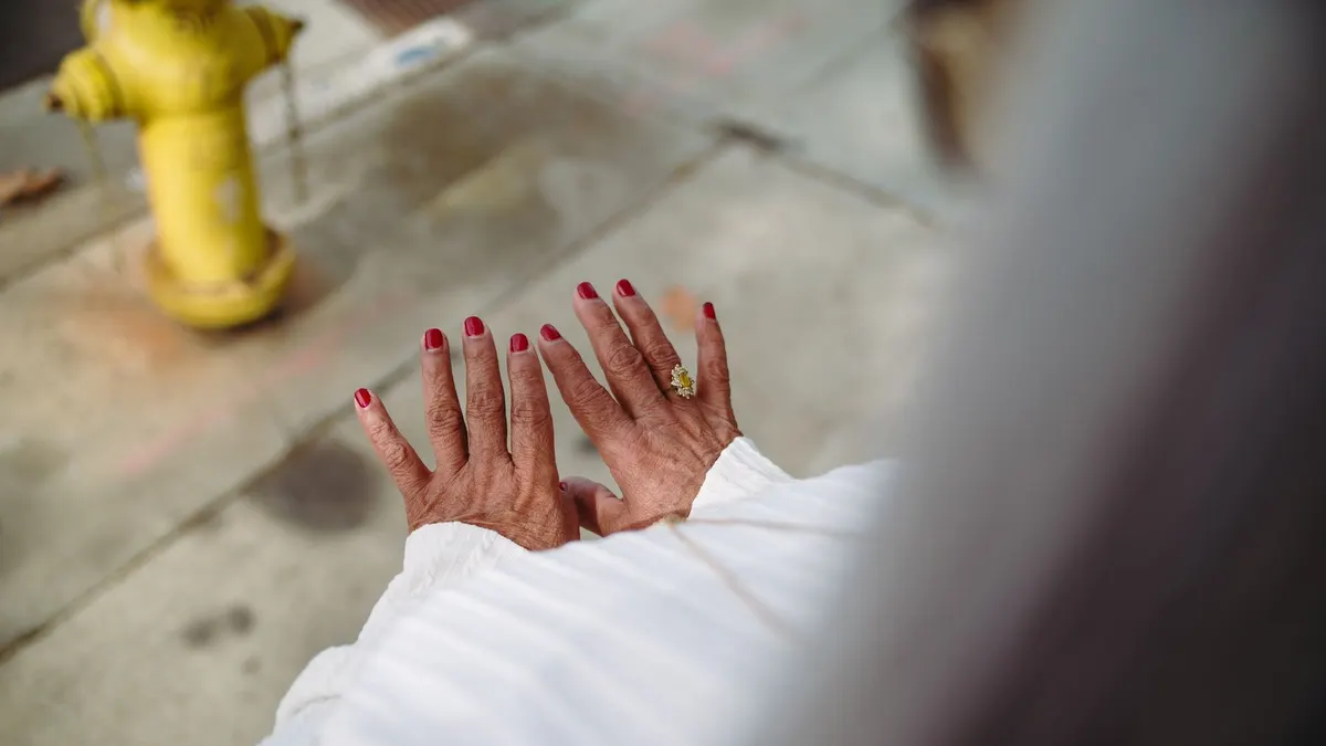 An elegant close-up of hands with red nail polish and jewelry, set against an urban outdoor backdrop.