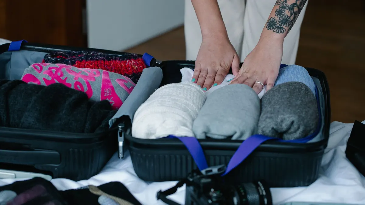 A person neatly packs clothes into luggage in a well-organized manner indoors.
