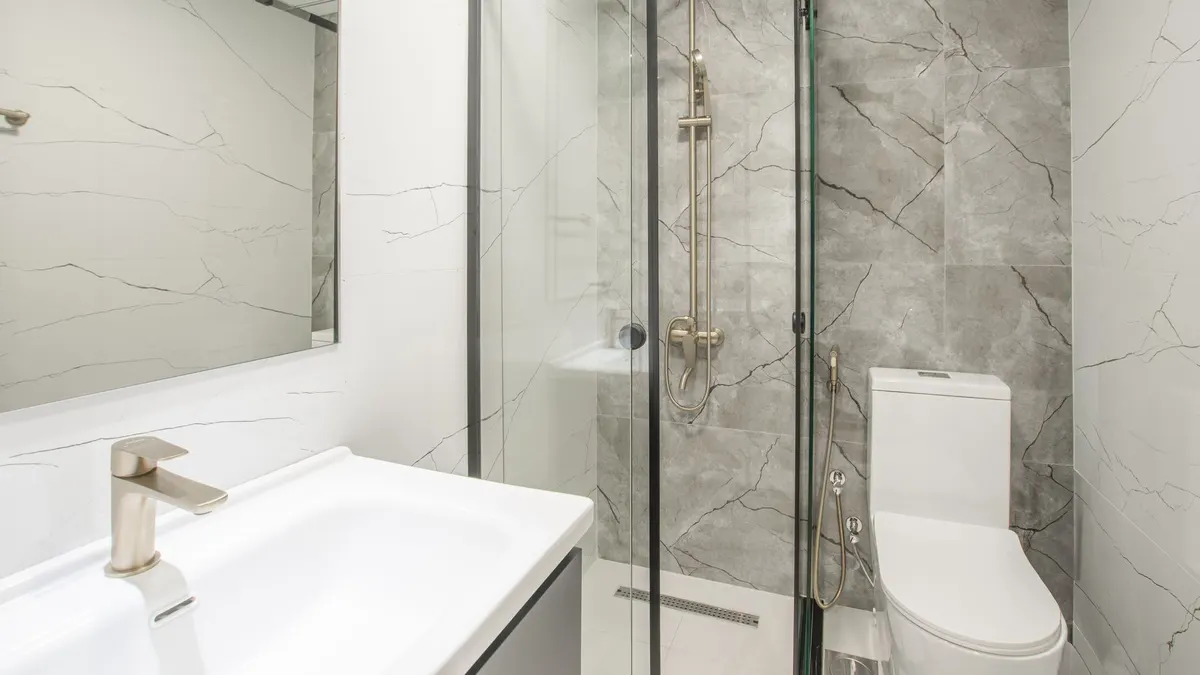 Bright modern bathroom featuring a glass shower, marble tiles, and sleek fixtures.
